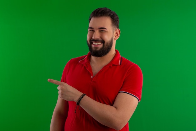 Hombre brasileño con barba con una camisa roja en una foto de estudio con un fondo verde ideal para recortar
