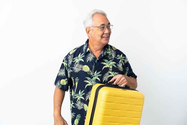 Hombre brasileño de mediana edad aislado sobre fondo blanco en vacaciones con maleta de viaje