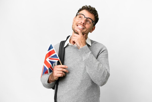 Hombre brasileño que sostiene una bandera del Reino Unido sobre un fondo blanco aislado mirando hacia arriba mientras sonríe