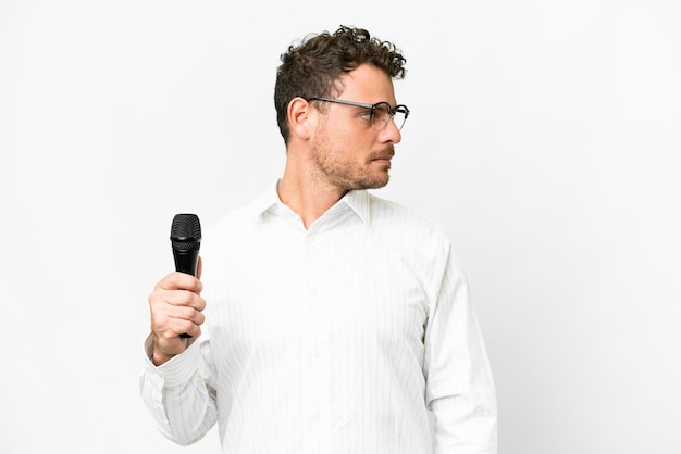 Hombre brasileño recogiendo un micrófono sobre un fondo blanco aislado mirando hacia un lado