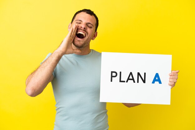 Hombre brasileño sobre fondo púrpura aislado sosteniendo un cartel con el mensaje PLAN A y gritando