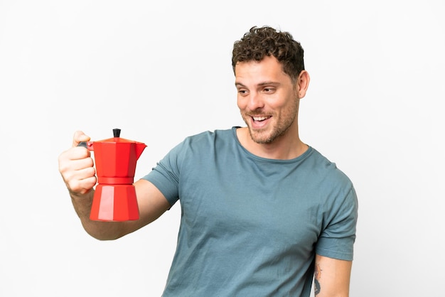 Hombre brasileño sosteniendo una cafetera sobre un fondo blanco aislado con expresión feliz