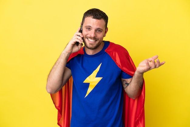 Hombre brasileño de superhéroe aislado sobre fondo amarillo manteniendo una conversación con el teléfono móvil con alguien