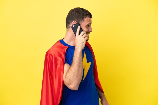 Hombre brasileño de superhéroe aislado sobre fondo amarillo manteniendo una conversación con el teléfono móvil con alguien