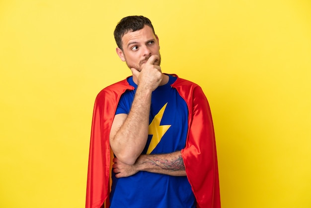 Hombre brasileño de superhéroe aislado sobre fondo amarillo que tiene dudas y con expresión de la cara confusa