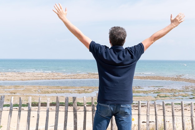 Hombre con los brazos en el aire en la vista trasera trasera en verano en la playa de Ile de Re