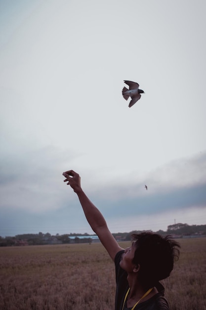 Foto hombre con los brazos levantados mientras el pájaro vuela en el campo contra el cielo