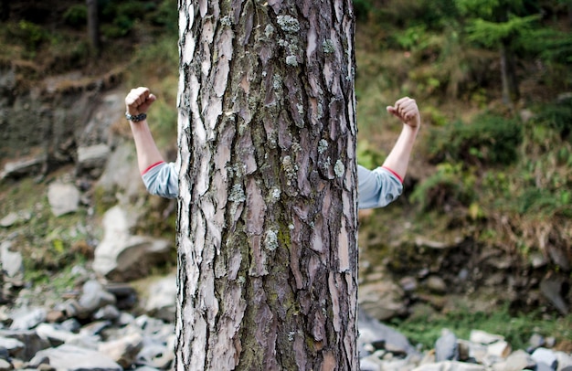 Hombre con los brazos levantados en el tronco del árbol