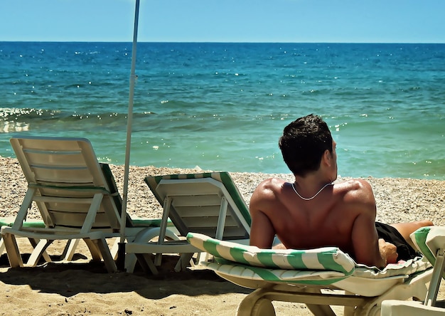 un hombre bronceado, un deportista, yace y descansa en una playa de arena del sur y mira al mar