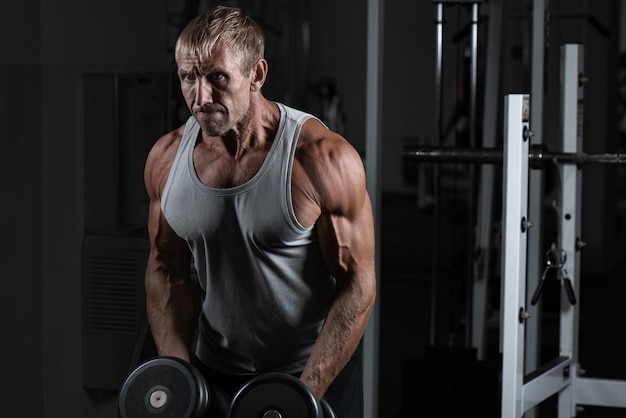 Hombre brutal adulto musculoso con pesas bombas bíceps en el gimnasio Retrato de culturista auténtico caucásico haciendo ejercicios de entrenamiento