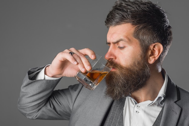 Hombre brutal de alcohol fuerte con vaso de degustación de whisky y degustación de hombre en traje bebe whisky