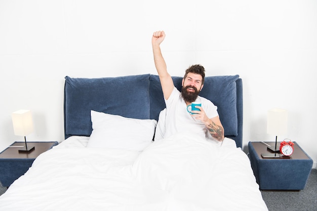 Hombre brutal guapo hipster dormitorio relajante beber café Chico barbudo disfrutar del café de la mañana Sintonizar el nuevo día Despertar mejor con una taza de café Relajarse y descansar La humanidad funciona con café