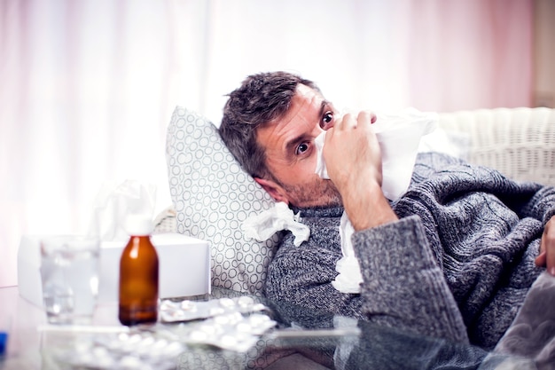 Foto hombre con bufanda azul contrajo gripe y sonarse la nariz en una servilleta. concepto de personas, salud y medicina