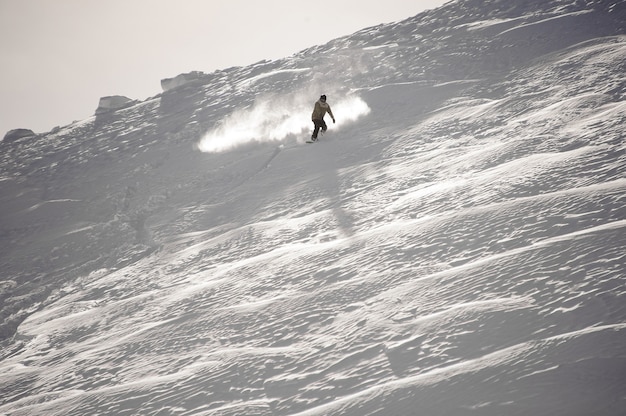 El hombre cabalgando por la colina cubierta de nieve en el snowboard en el popular complejo turístico de Gudauri en Georgia