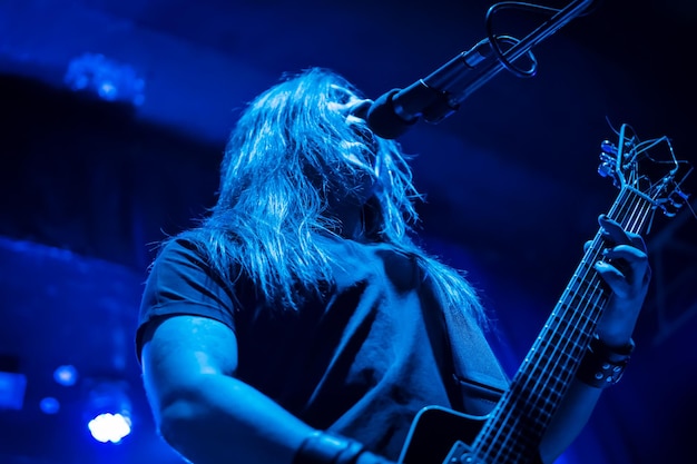 Hombre con cabello largo sostiene una guitarra y canta en un micrófono en un concierto, una vista desde abajo, primer plano