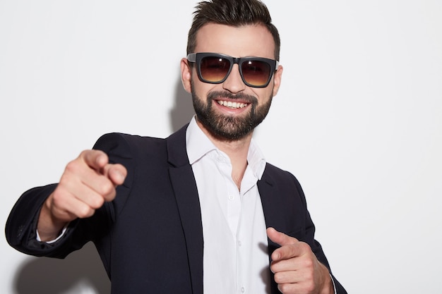 Hombre con cabello negro y barba con camisa blanca, traje y gafas de sol en el fondo blanco del estudio, retrato, feliz.