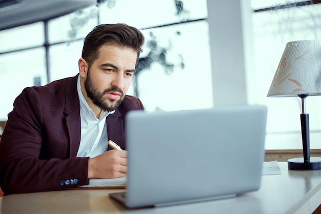 Foto un hombre de cabello negro hace un proyecto en la computadora. un hombre escribe ideas para una tarea en un cuaderno.