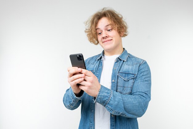 Hombre con cabello ondulado rubio juega un juego de teléfono en un teléfono inteligente sobre un fondo blanco.