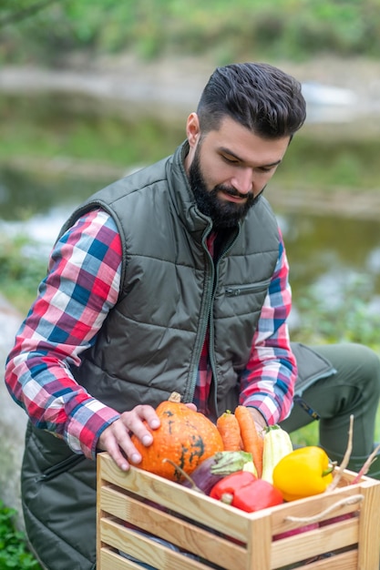 Un hombre de cabello oscuro con camisa a cuadros con una caja con verduras.