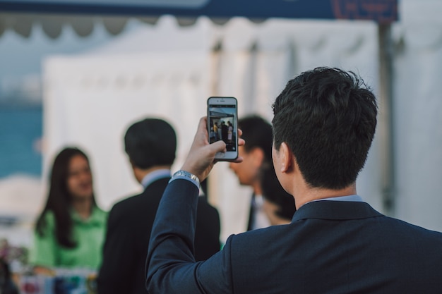 Foto hombre con cabello oscuro tomando fotos de personas en el teléfono inteligente