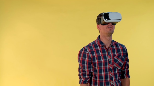 Foto hombre de cabello oscuro usando gafas de realidad virtual mientras está de pie contra un fondo amarillo que está bajo control...