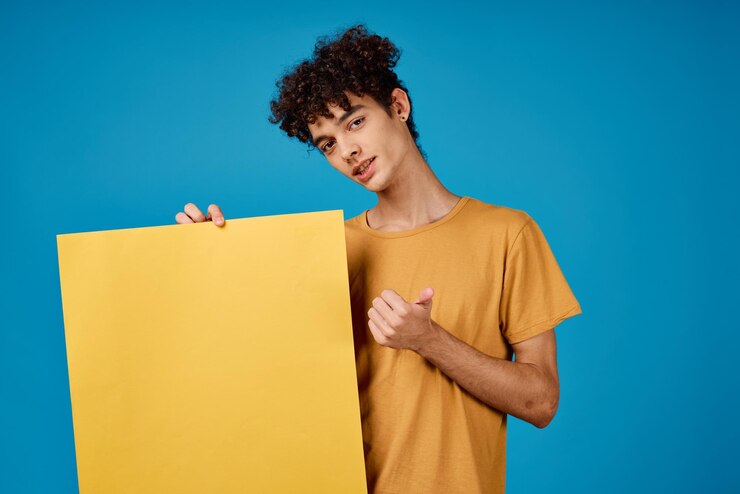 Foto hombre con cabello rizado sosteniendo un cartel amarillo en sus manos publicitando foto de alta calidad