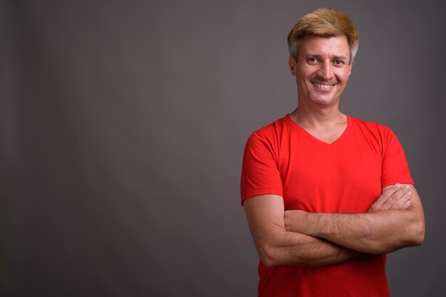 Hombre con cabello rubio vistiendo camisa roja contra la pared gris