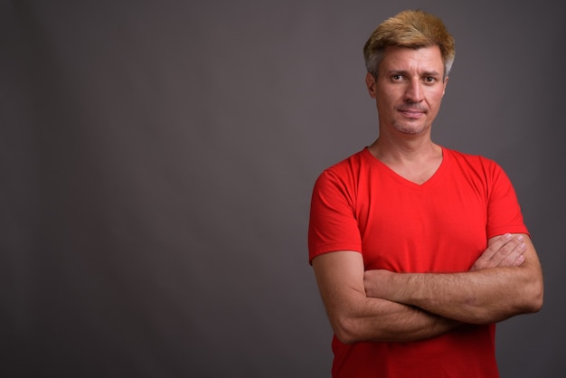 Hombre con cabello rubio vistiendo camisa roja contra la pared gris