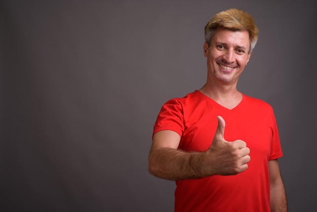 Foto hombre con cabello rubio vistiendo camisa roja contra la pared gris