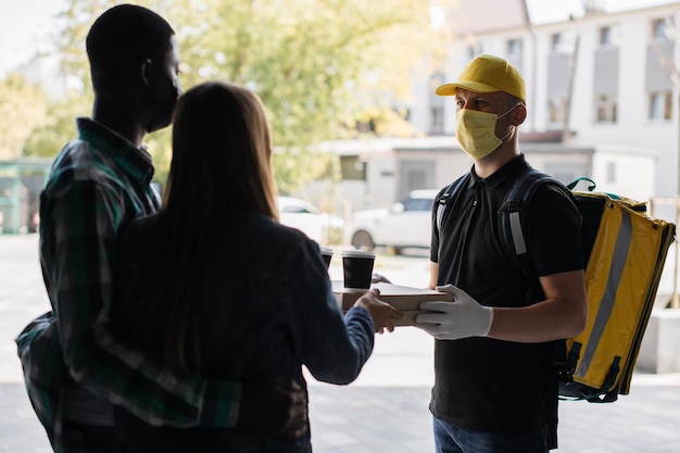 Hombre cacasiano con mascarilla trabaja en la entrega de pizza