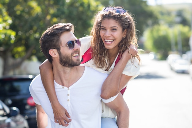 Hombre de la cadera que da piggy back a su novia en la calle