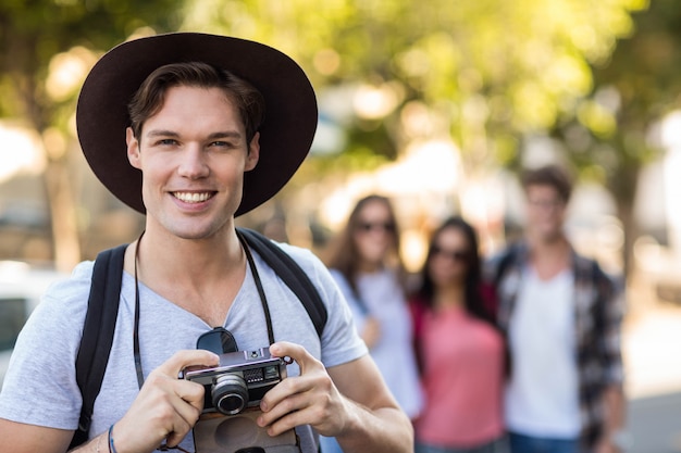 Hombre de cadera sosteniendo una cámara digital y sonriendo a la cámara