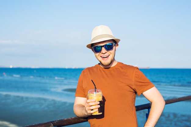 Hombre con café frappe cerca del mar sintiéndose libre disfrutando de las vacaciones de tiempo libre