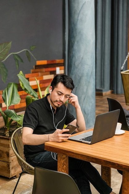 Hombre en una cafetería sentado usando un teléfono celular y escuchando música.