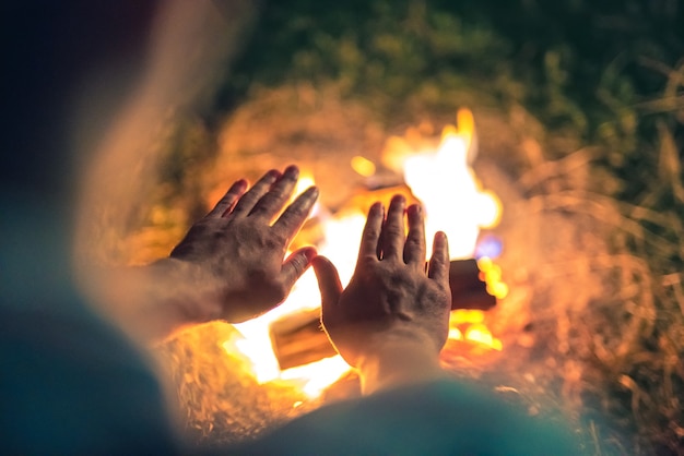 El hombre calentando las manos cerca de la hoguera. Noche