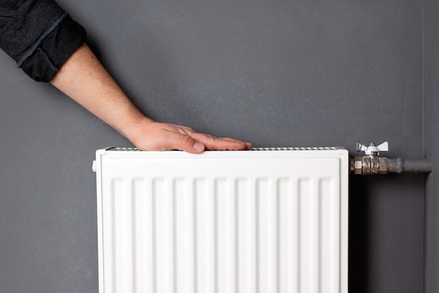Hombre calentando las manos sobre el radiador de calefacción cerca de la pared gris, primer plano