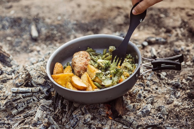 Foto el hombre se calienta en un fuego y cocina en un campamento de verano