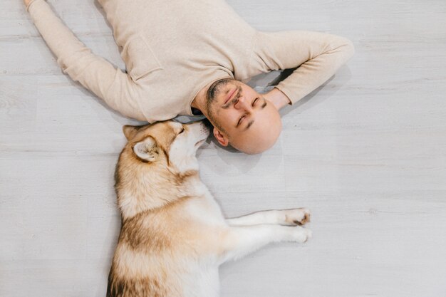 Hombre calvo adulto con cachorro husky durmiendo en el piso.