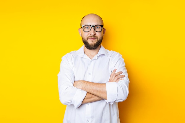 Hombre calvo con barba con gafas en una camisa blanca sobre un fondo amarillo