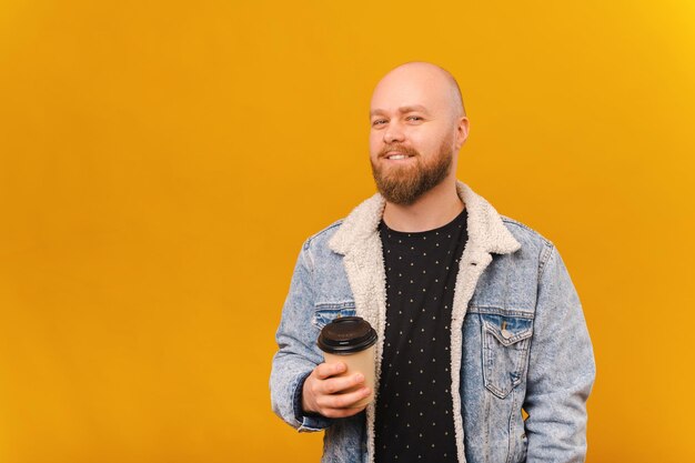 El hombre calvo barbudo extasiado está sosteniendo una taza de papel para llevar de café caliente