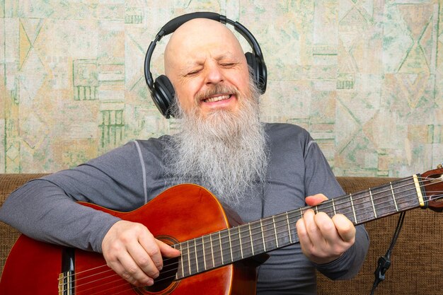 El hombre calvo barbudo toca la guitarra clásica.