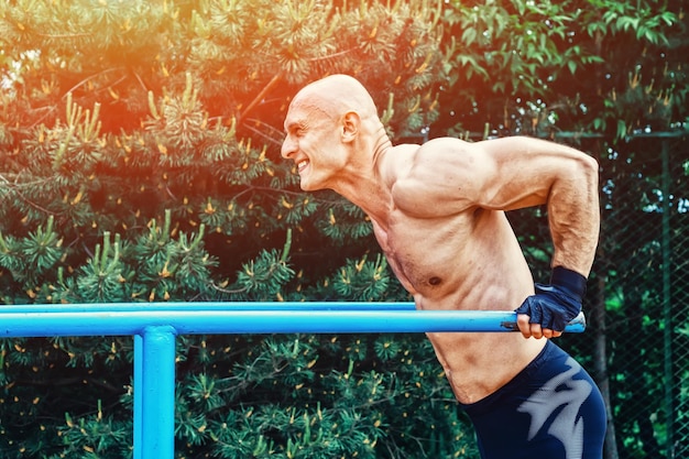 Hombre calvo haciendo flexiones en barras paralelas en un parque