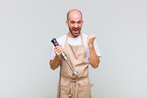 Hombre calvo joven que se siente sorprendido, emocionado y feliz, riendo y celebrando el éxito, diciendo ¡guau!