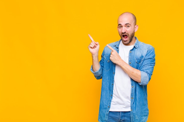 Hombre calvo que se siente alegre y sorprendido, sonriendo con una expresión de sorpresa y apuntando hacia un lado