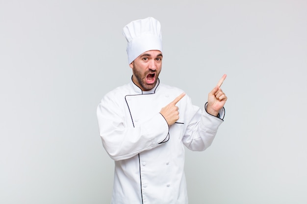 Hombre calvo que se siente alegre y sorprendido, sonriendo con una expresión de sorpresa y apuntando hacia un lado