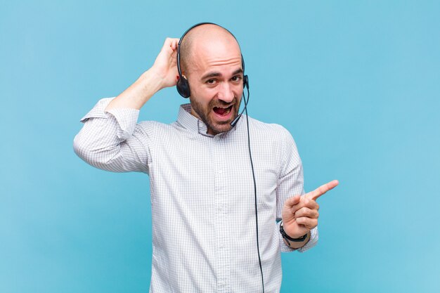 Hombre calvo riendo, luciendo feliz, positivo y sorprendido, dándose cuenta de una gran idea apuntando al espacio de copia lateral