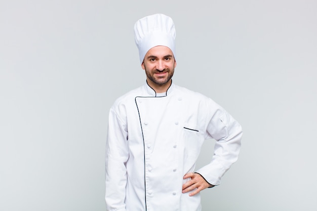 Hombre calvo sonriendo felizmente con una mano en la cadera y actitud confiada, positiva, orgullosa y amistosa