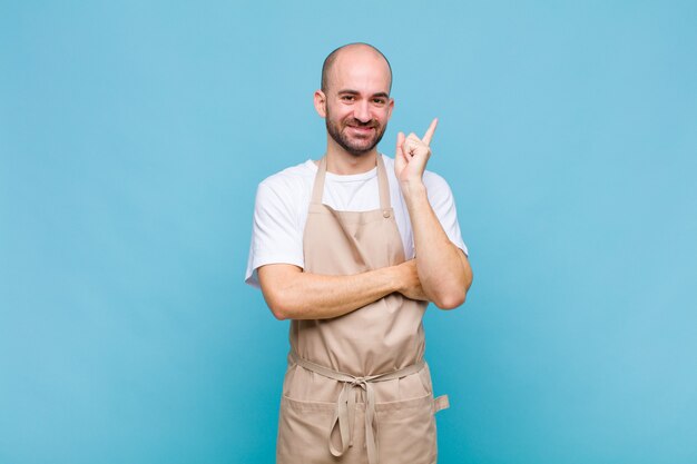 Hombre calvo sonriendo felizmente y mirando hacia los lados, preguntándose, pensando o teniendo una idea