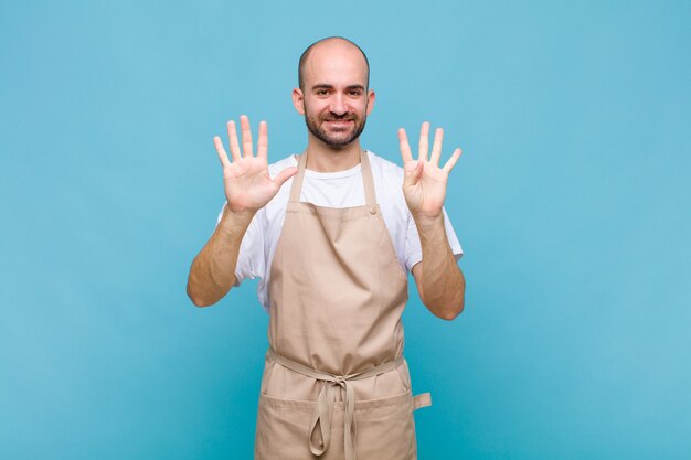 Hombre calvo sonriendo y mirando amigable, mostrando el número nueve o noveno con la mano hacia adelante, contando hacia atrás