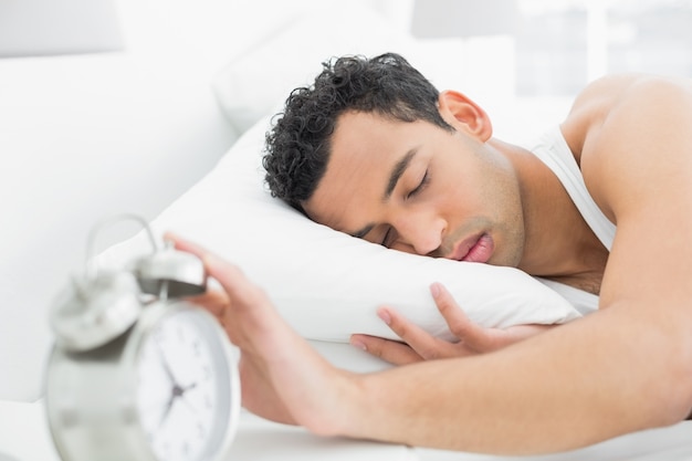 Hombre en la cama extendiendo la mano al despertador